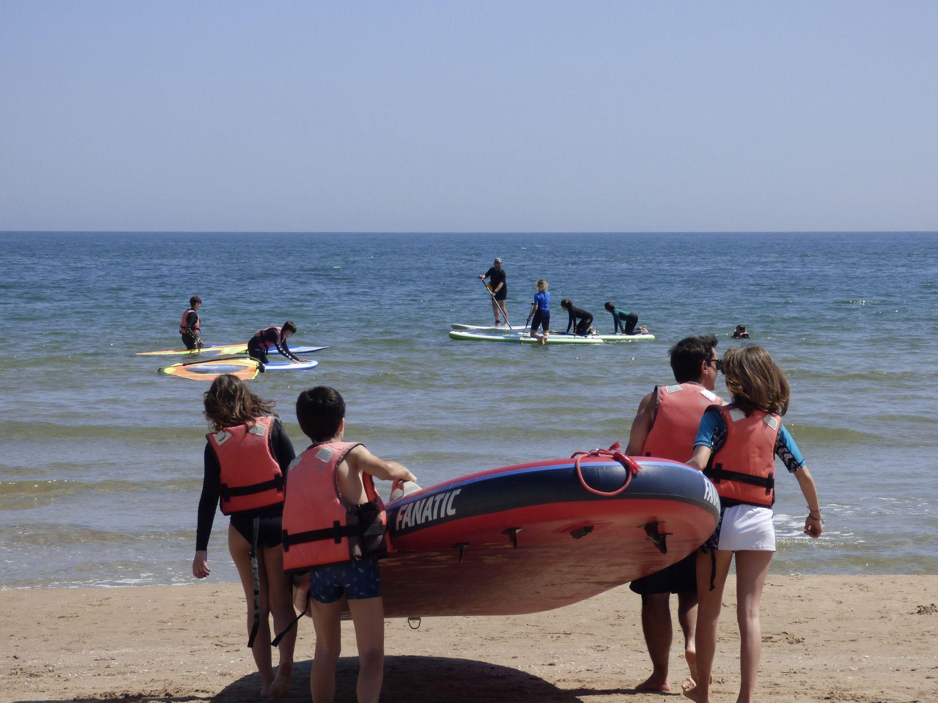 Alumnos llevan juntos una tabla hacia el mar durante una actividad de Ohana